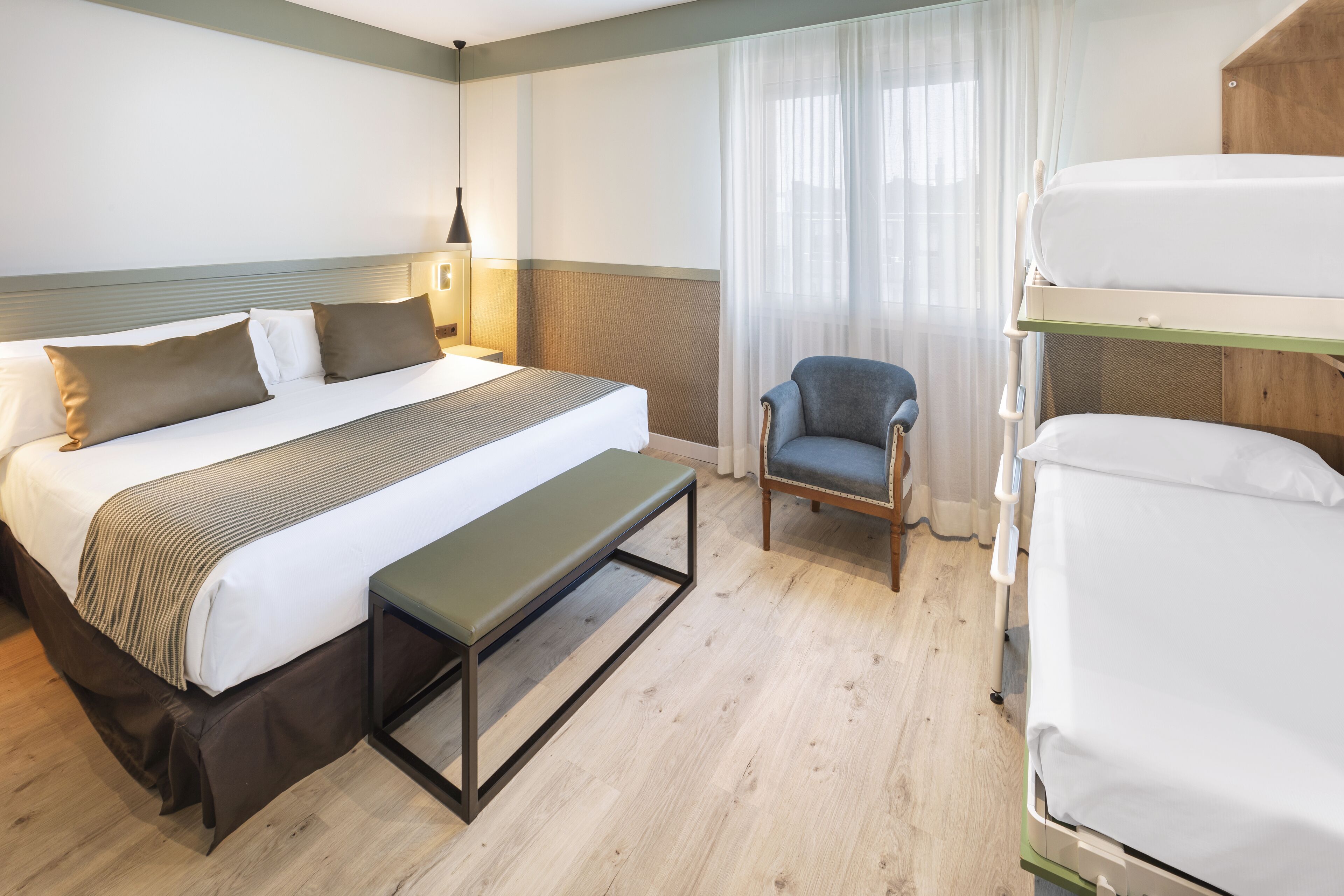 A hotel room with a bed, a bench, a chair, and a bunk bed.