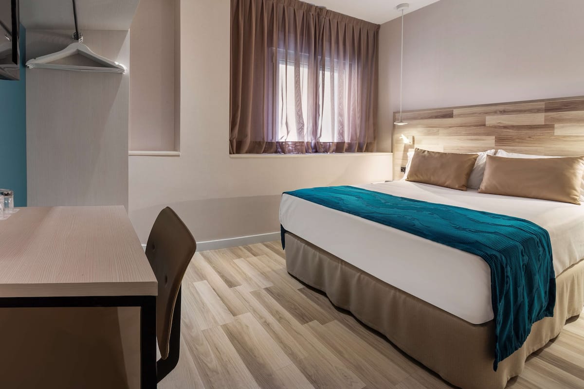 Quarto de hotel com cama, mesa e cadeira.