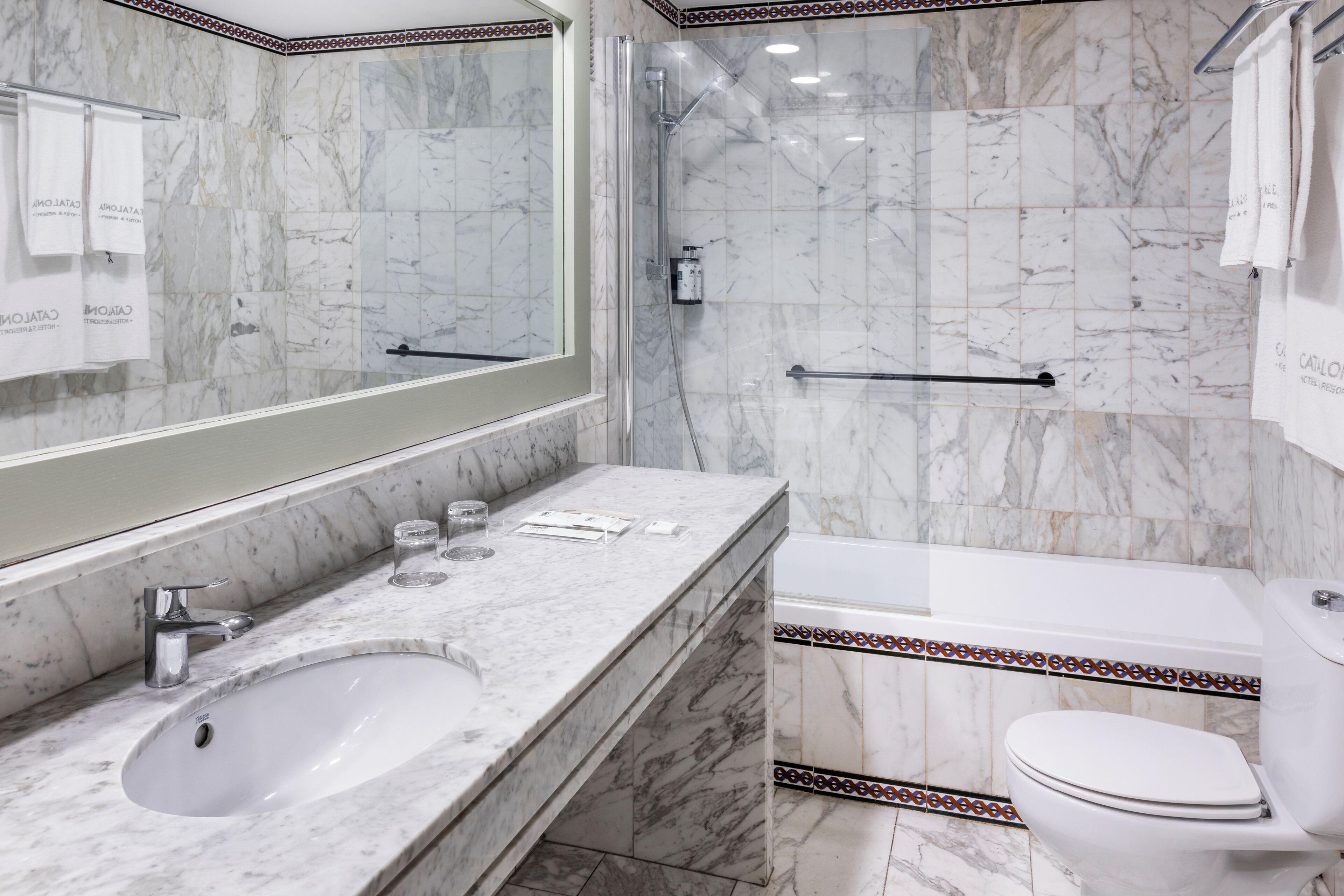A marble bathroom with a sink, mirror, shower, and toilet.