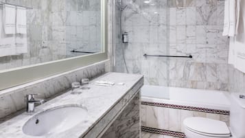 A marble bathroom with a sink, mirror, shower, and toilet.