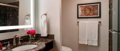 A bathroom with a marble sink, a toilet, and a shower area.