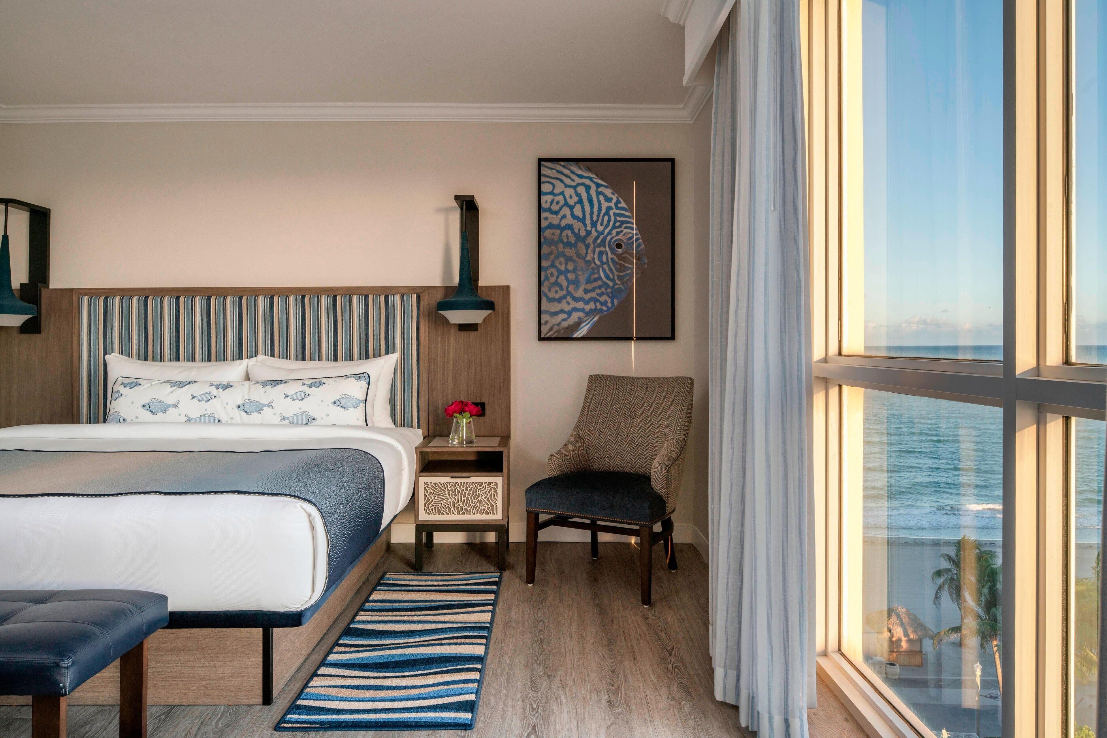 A hotel room with a large bed, a chair, a nightstand, and a view of the ocean.