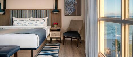 A hotel room with a large bed, a chair, a nightstand, and a view of the ocean.