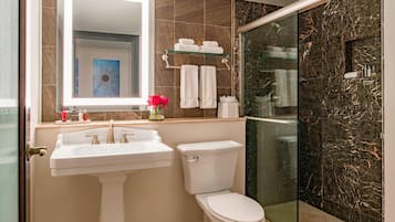 A bathroom with a white sink, a toilet, a glass shower enclosure, and a marble-tiled wall.
