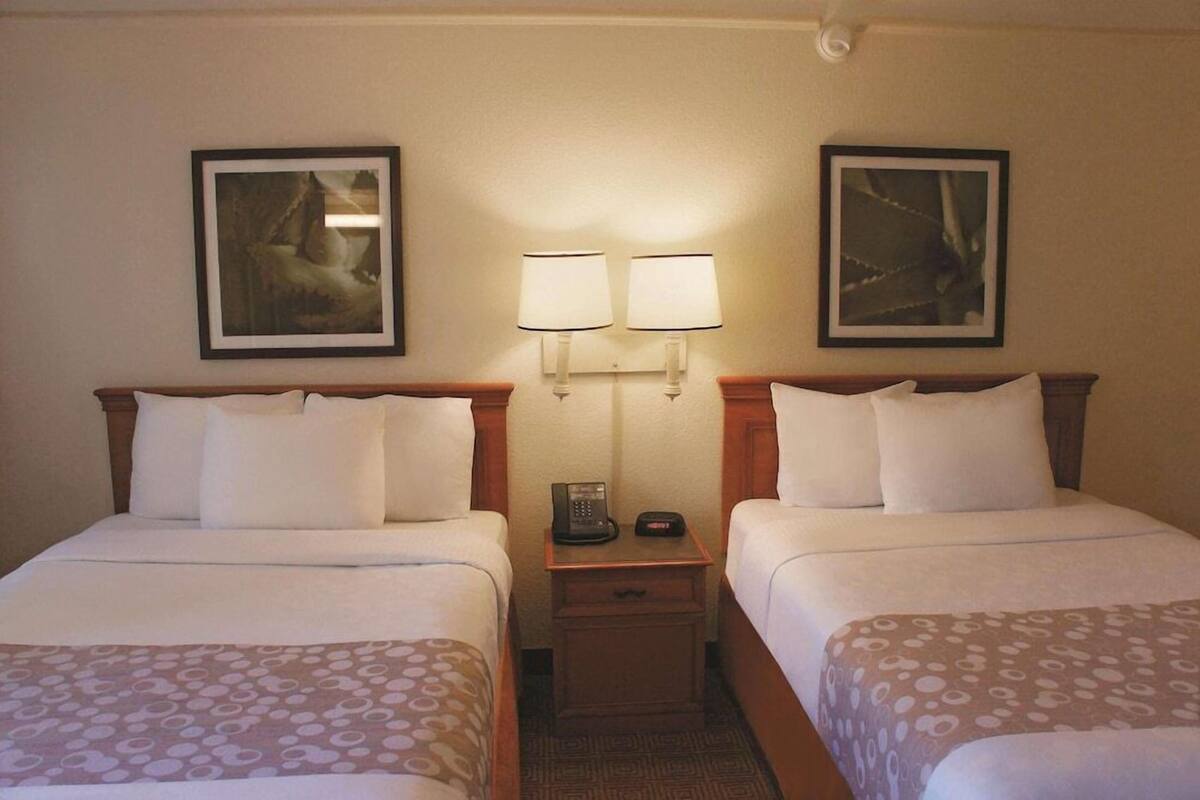 A hotel room with two beds, a nightstand with a phone, and two wall-mounted lamps.