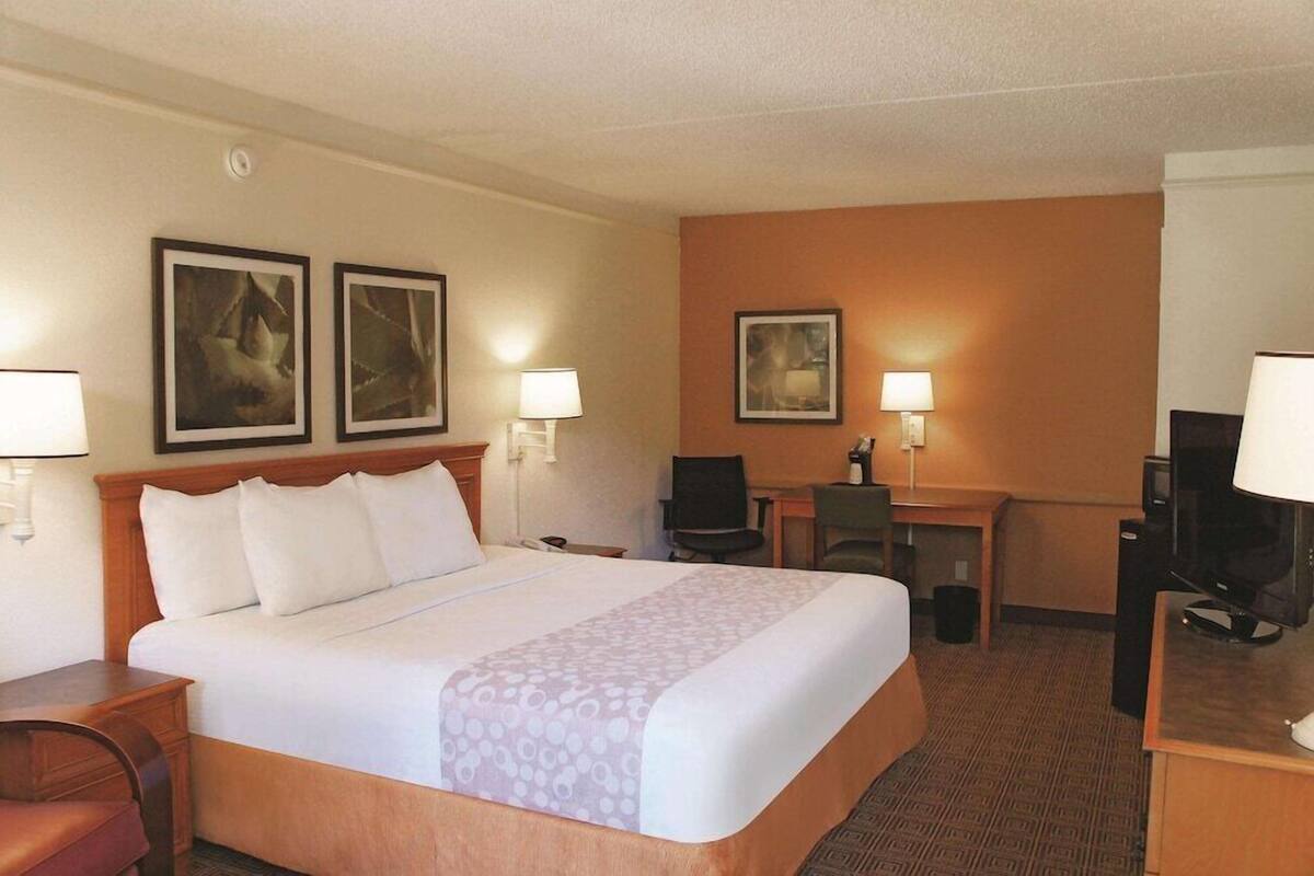 A hotel room with a bed, desk, two chairs, and a television.