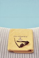 A folded yellow towel with sunglasses and the text "AEROPOSTAL HILL" on a wicker surface.