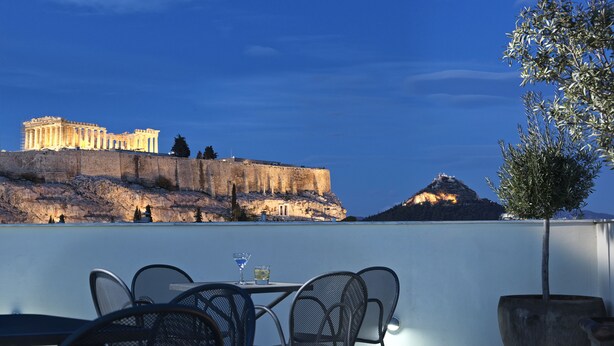 Une terrasse avec des places assises extérieures, offrant une vue sur d’anciennes ruines et une montagne.