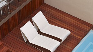 Un espace piscine moderne avec une terrasse en bois et deux chaises longues blanches.