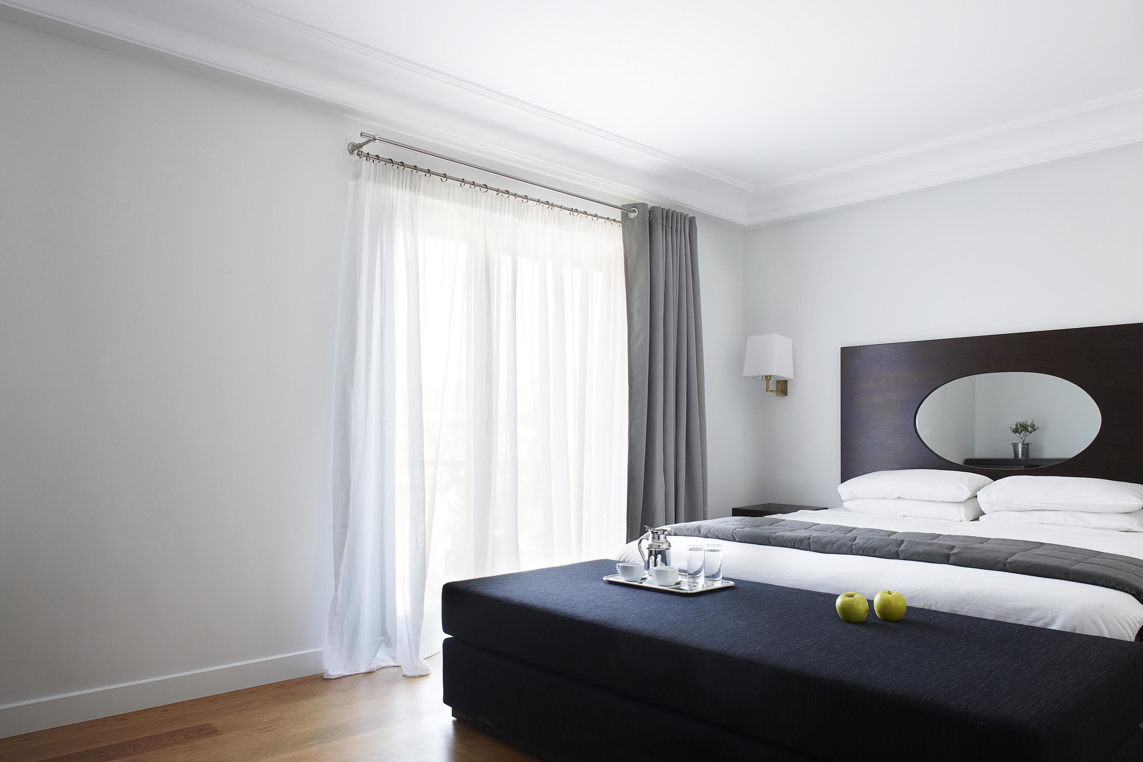 Une chambre d’hôtel moderne avec un grand lit, une table de chevet, un miroir et une fenêtre avec des rideaux.