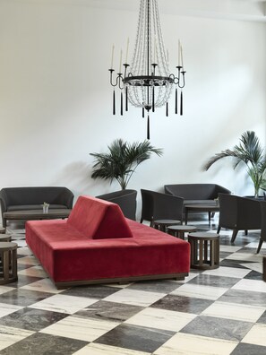 Un área de estar moderna con un sofá rojo, sillones negros, una araña y plantas en macetas.