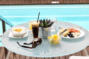 Una mesa de vidrio con comida y bebidas cerca de una piscina.