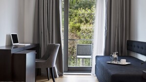 Une chambre d'hôtel moderne équipée d'un bureau, d'un ordinateur portable, d'une chaise grise et d'un lit sur lequel se trouve un plateau avec des articles pour le petit-déjeuner.