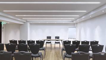 Un salón de conferencias con una larga mesa, varias sillas, una pizarra y iluminación empotrada.
