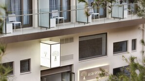 Un hôtel à plusieurs étages au design moderne, doté de balcons avec des garde-corps en verre et des chaises blanches.
