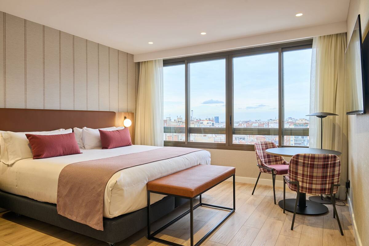 A hotel room with a large bed, a bench, a table, and two chairs.