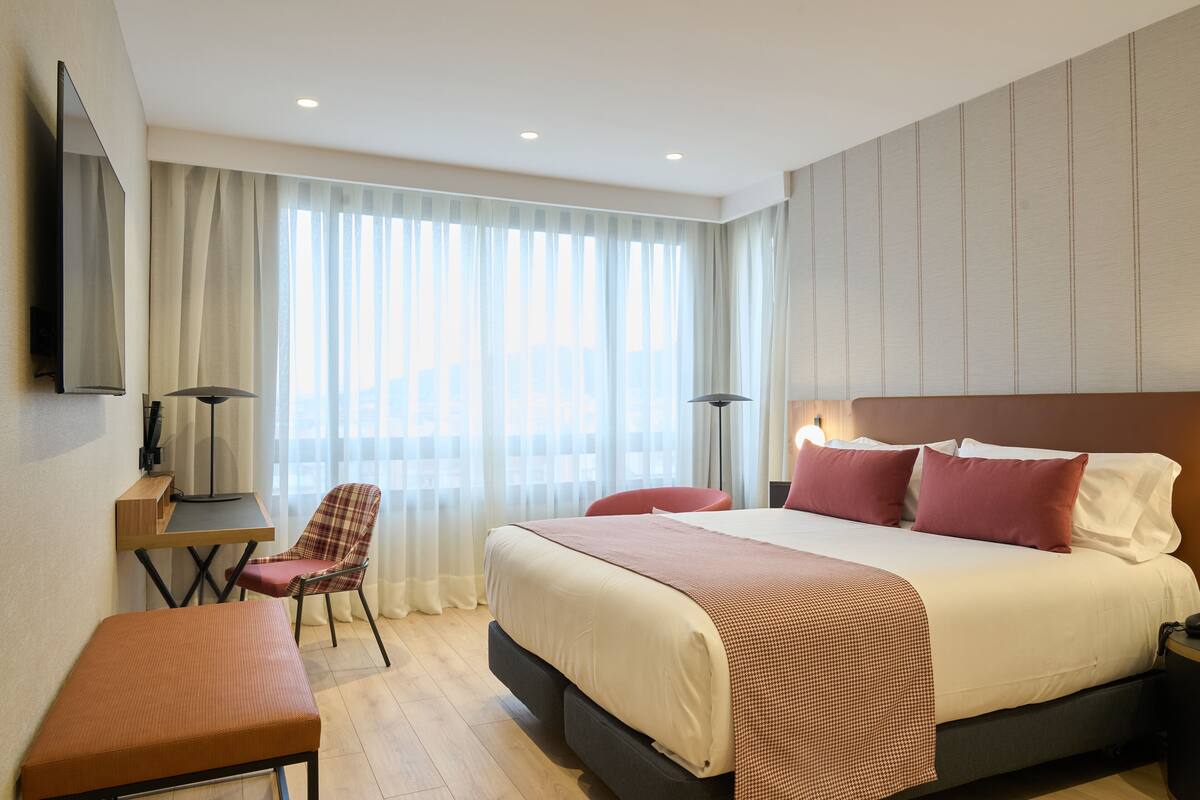 A modern hotel room with a large bed, a desk, a chair, and a flat-screen TV.