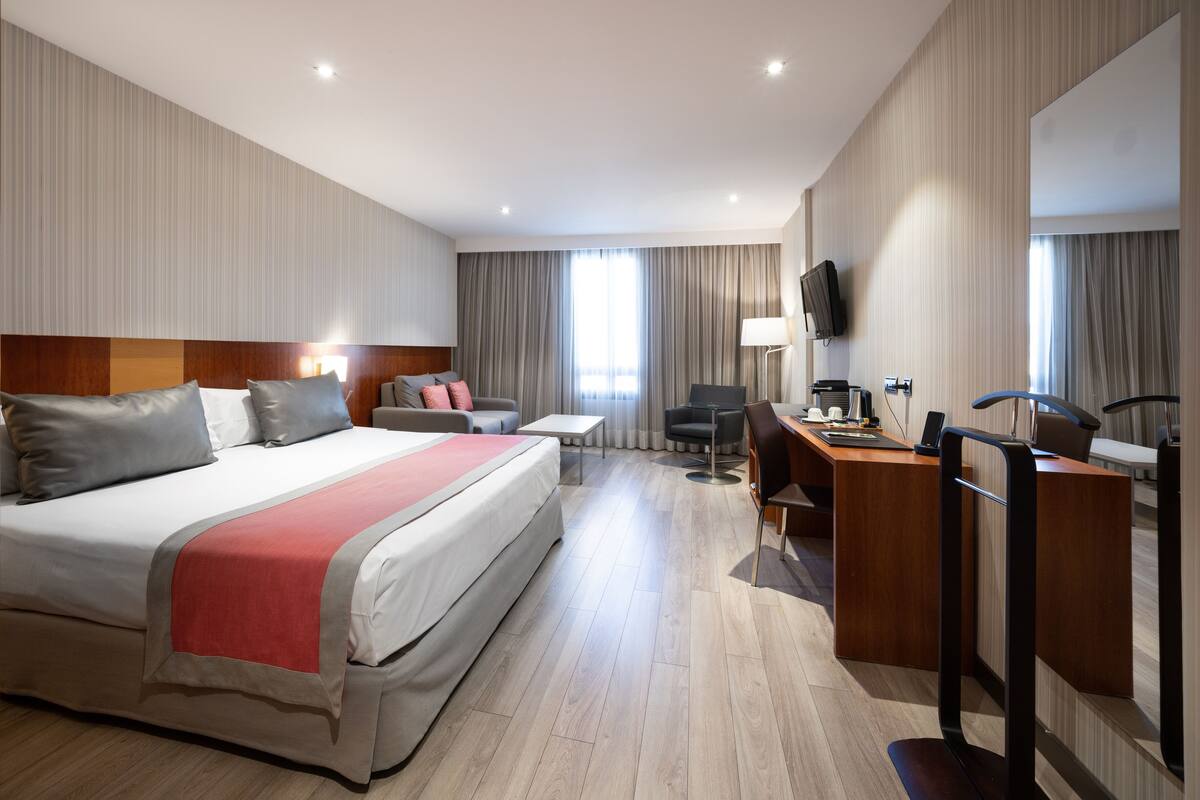 A hotel room with a large bed, a desk, a chair, a television, and a window with curtains.