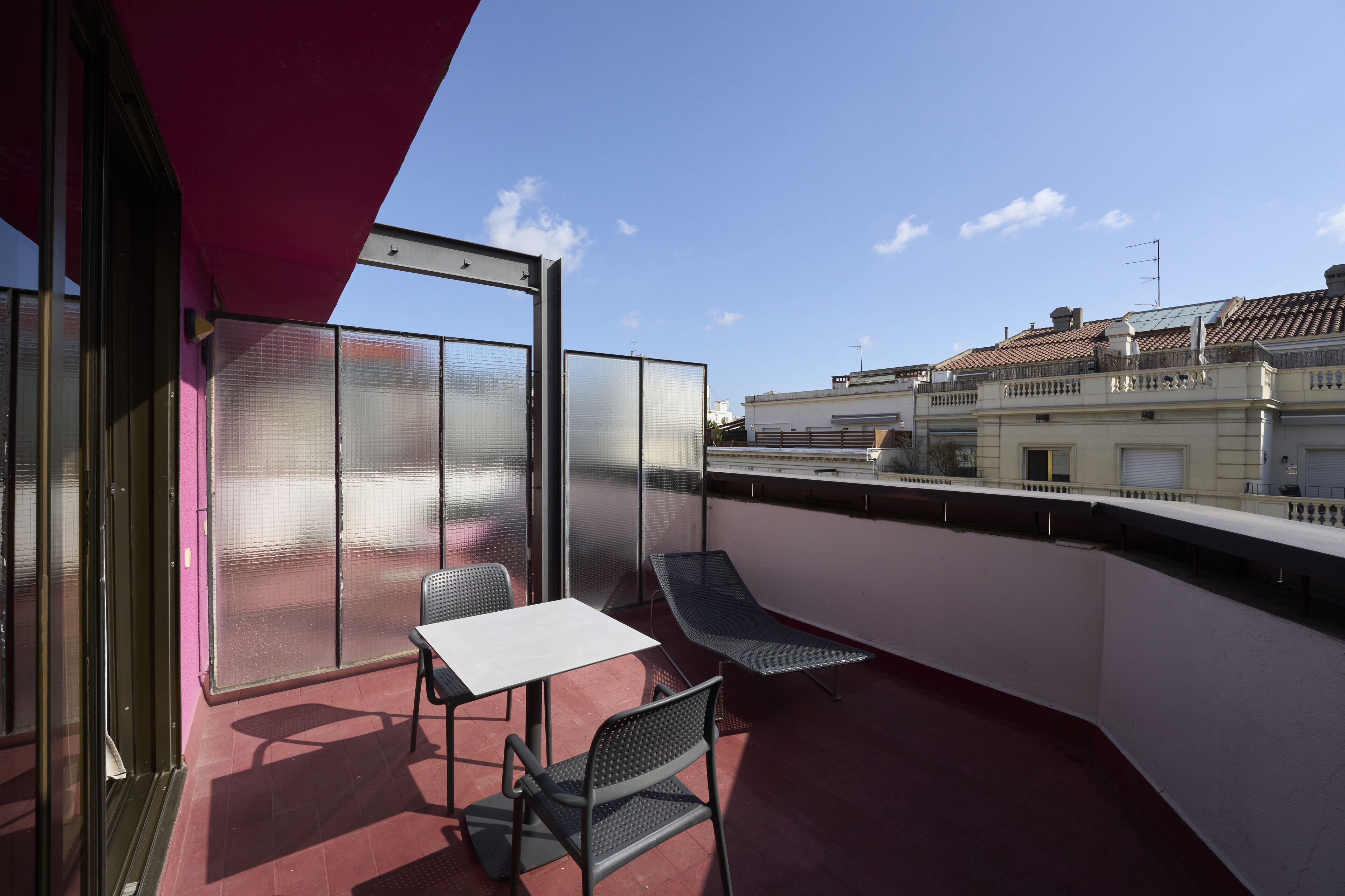 A balcony with a table and chairs, a red awning, and a view of buildings in the background.