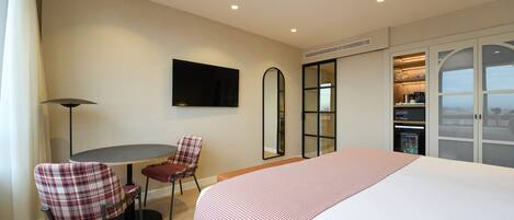 A hotel room with a large bed, a dining table with chairs, a TV mounted on the wall, and a wardrobe with a sliding door.