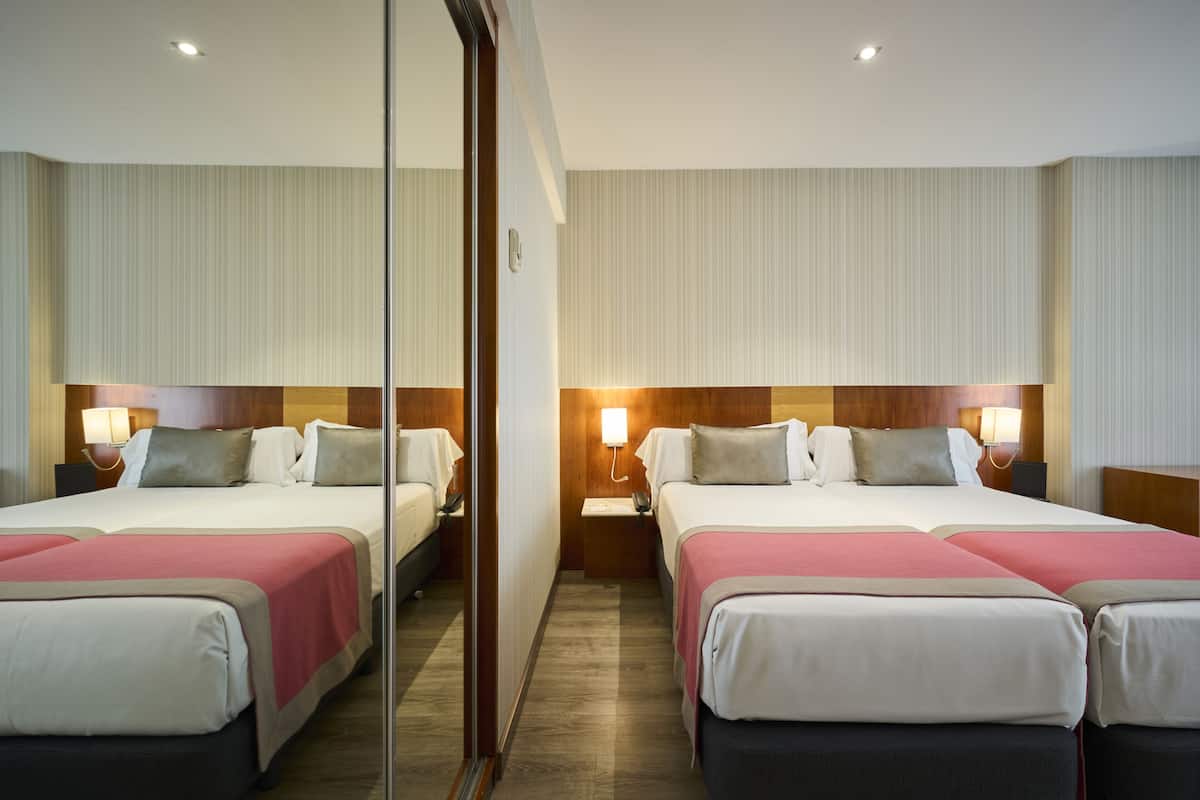 A hotel room with two beds, each with a nightstand, bedside lamp, and a mirror.
