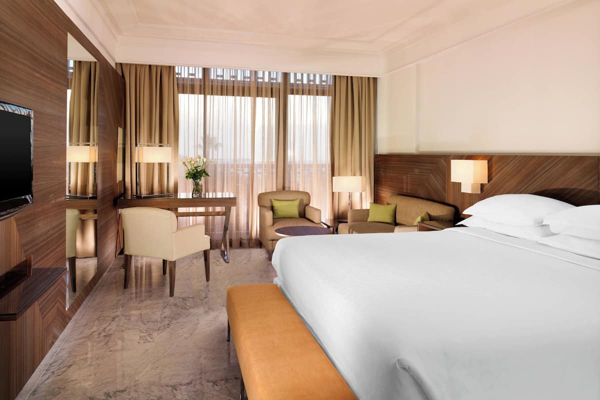 A hotel room with a large bed, a desk with a chair, a TV, and a window with curtains.