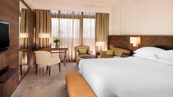 A hotel room with a large bed, a desk with a chair, a TV, and a window with curtains.