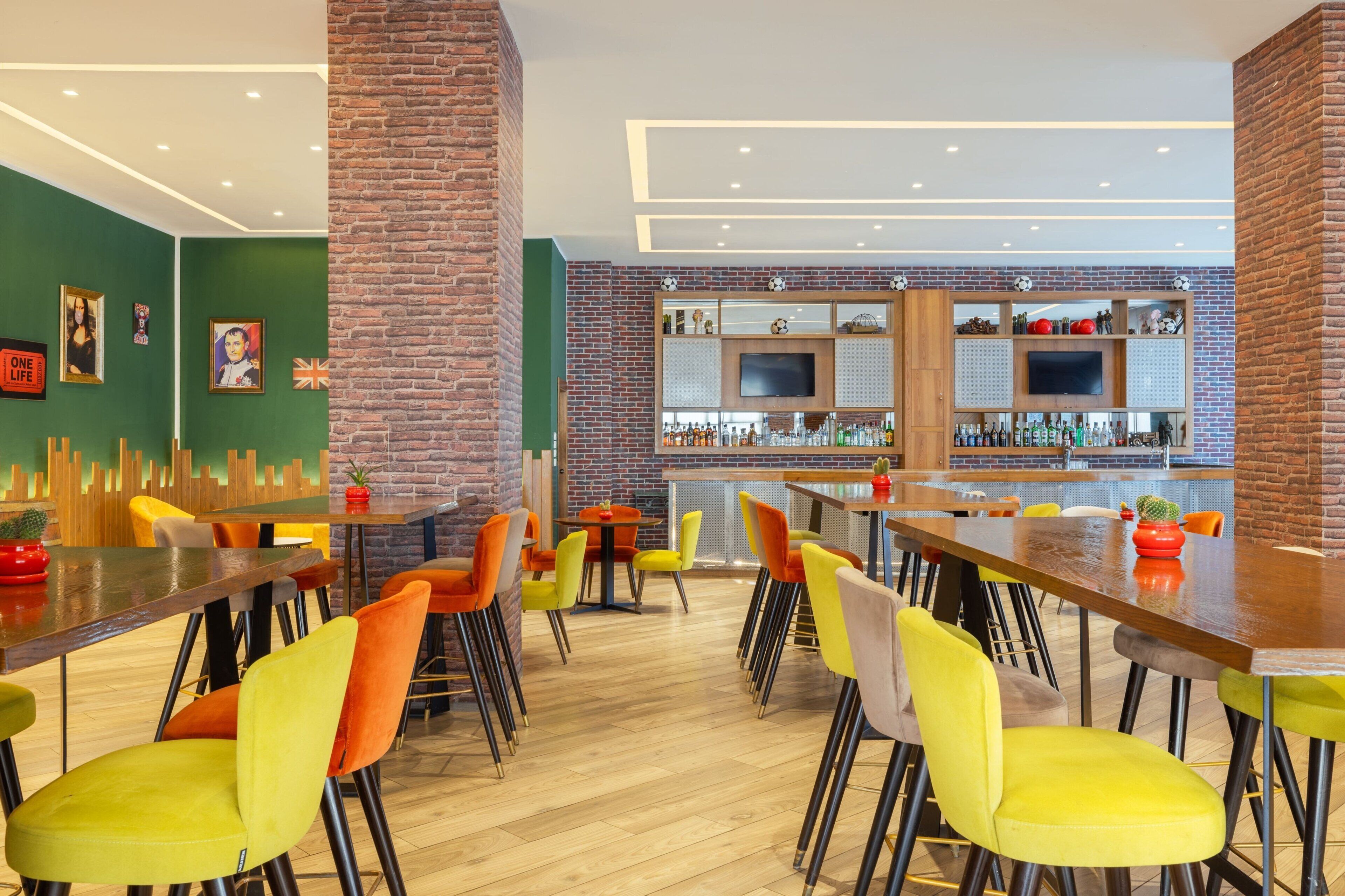 Uma área de bar moderna com mesas de madeira, cadeiras coloridas e um painel de parede de tijolos.