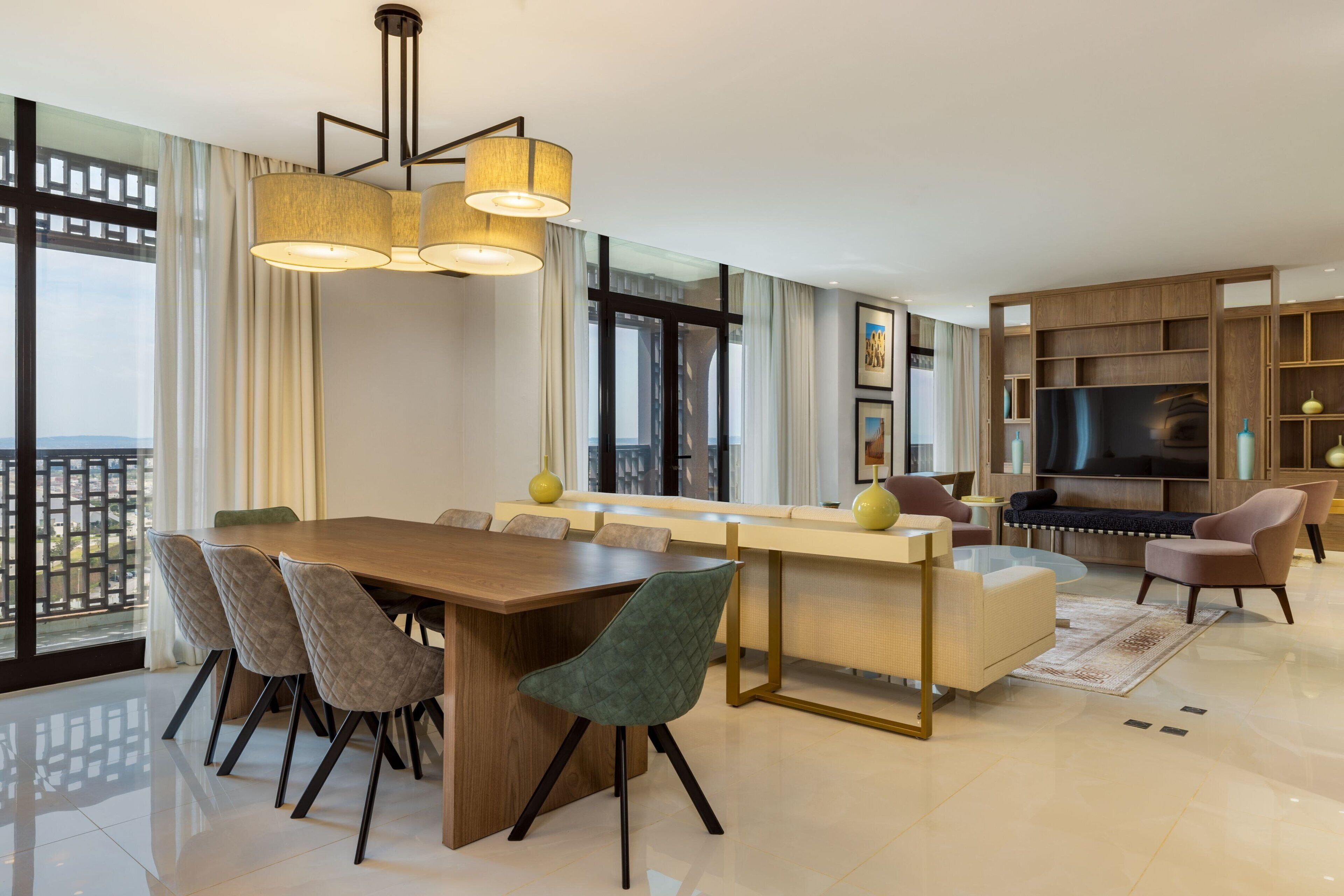 A modern living room with a wooden dining table, cushioned chairs, a sofa, and a TV.