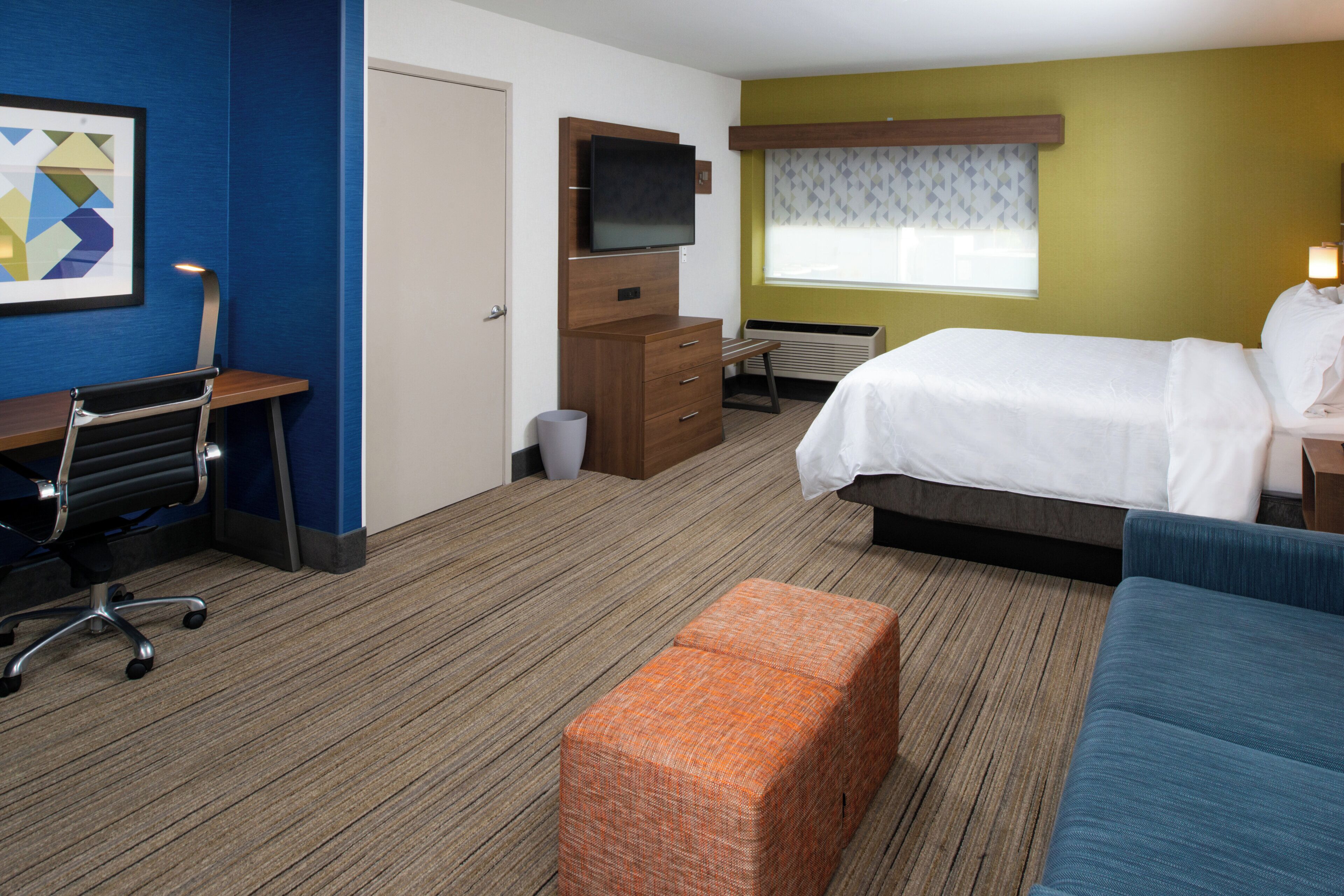 Una habitación de hotel con una cama, un escritorio, una silla, un televisor y una ventana con cortinas estampadas.