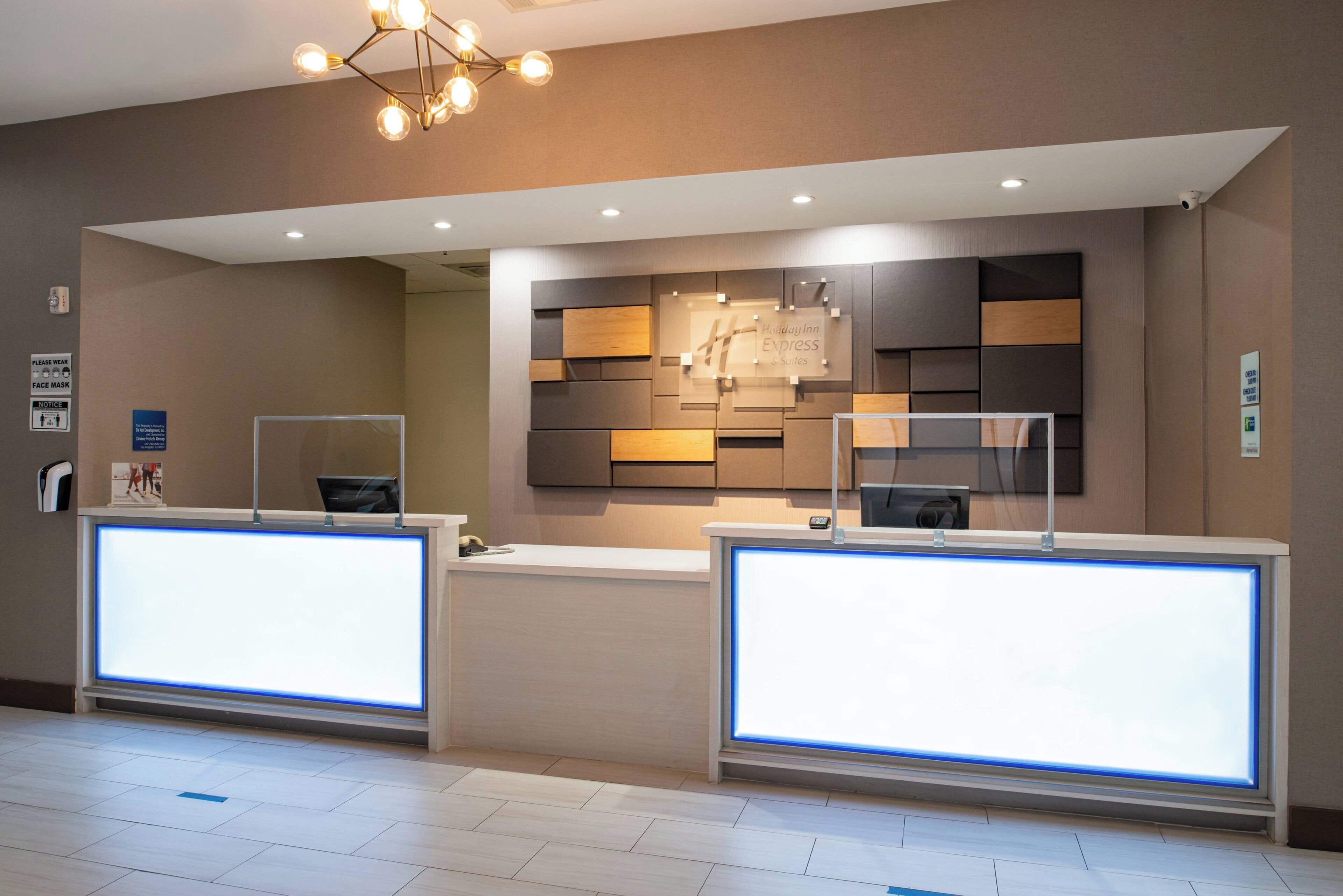 A hotel reception area with two reception desks, a modern light fixture, and a wall-mounted display.