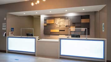 A hotel reception area with two reception desks, a modern light fixture, and a wall-mounted display.