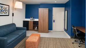 A modern room with a blue wall, a wooden wardrobe, a white door, a blue sofa, an orange ottoman, and a desk with a chair. - Holiday Inn Express & Suites Los Angeles Downtown West by IHG (Los Angeles)