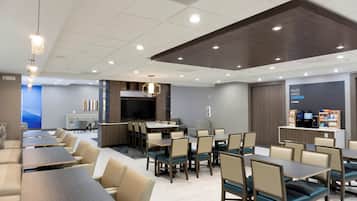 En modern hotellrestaurang med flera bord och stolar, en bardisk och en stor skärm.