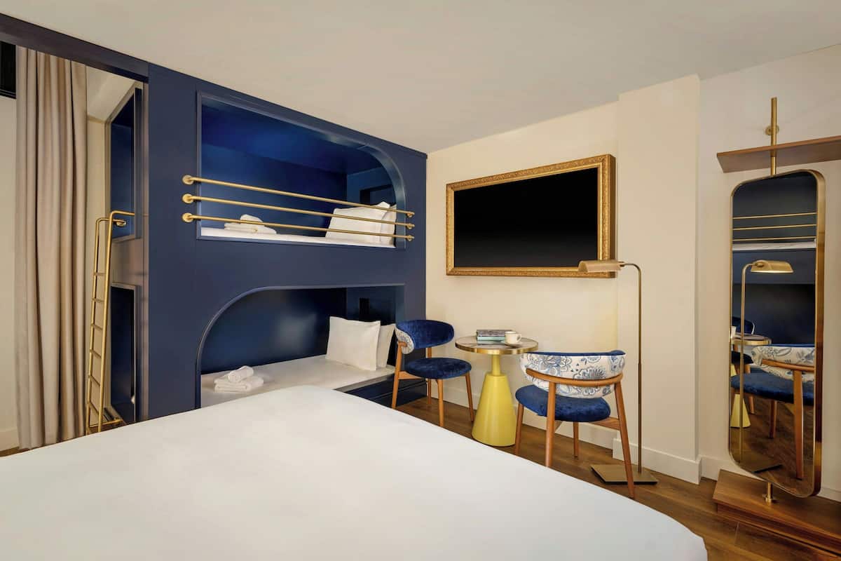 Ein Hotelzimmer mit einem Etagenbett, einem Schreibtisch mit Stuhl, einem Spiegel und einem Nachttisch.