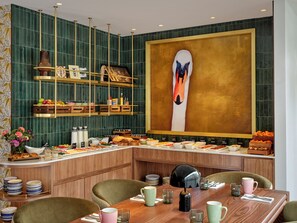 Een ontbijtbuffet met diverse gerechten, houten meubels en een groot abstract schilderij aan de muur.
