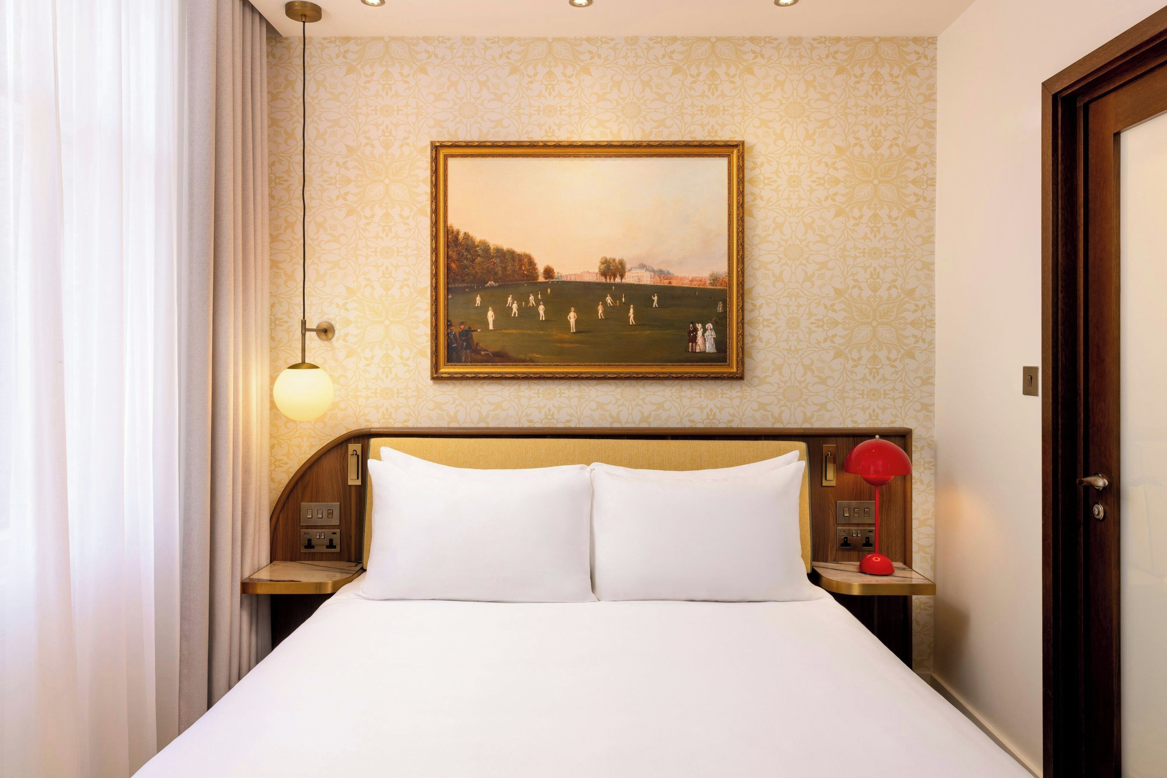 Een hotelkamer met een bed, een schilderij, een nachtkastje met een lamp en een deur.