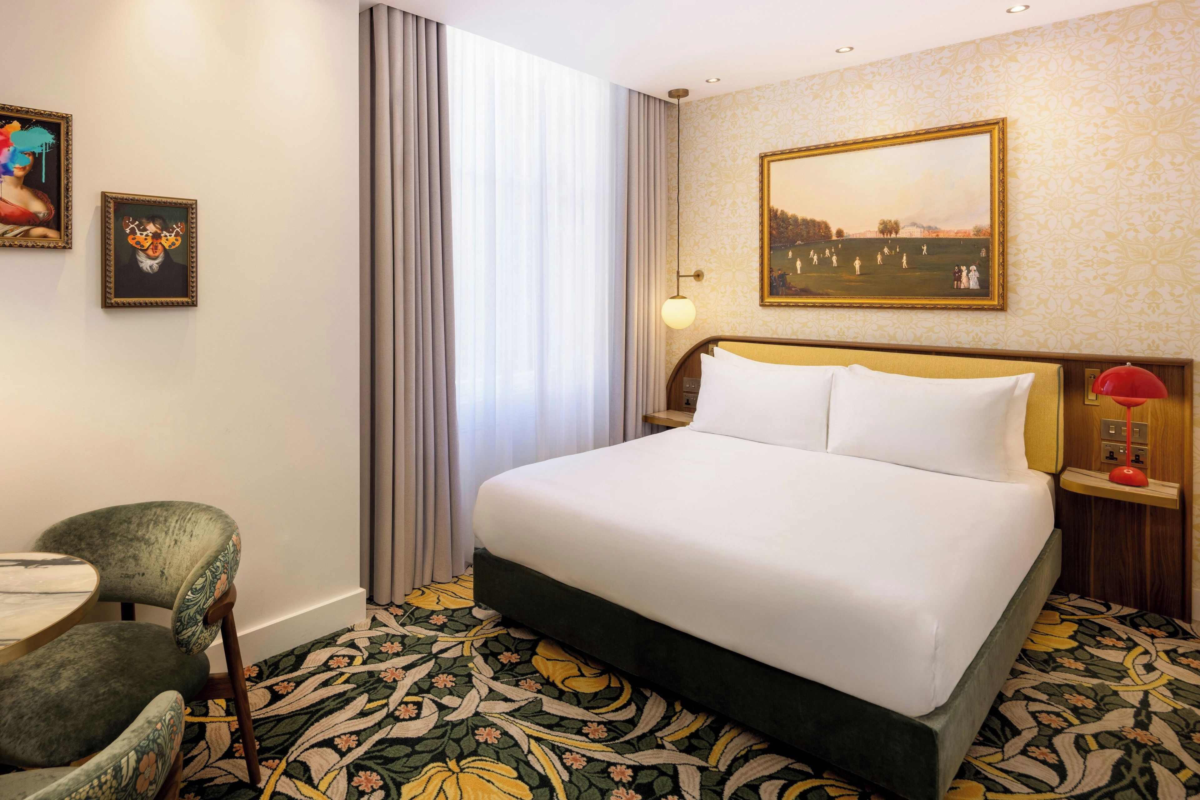 A hotel room with a large bed, a desk, a chair, a painting on the wall, and a patterned carpet.