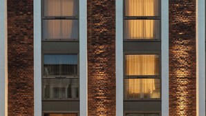 Fachada de hotel con revestimiento de ladrillo, varias ventanas y un toldo negro.