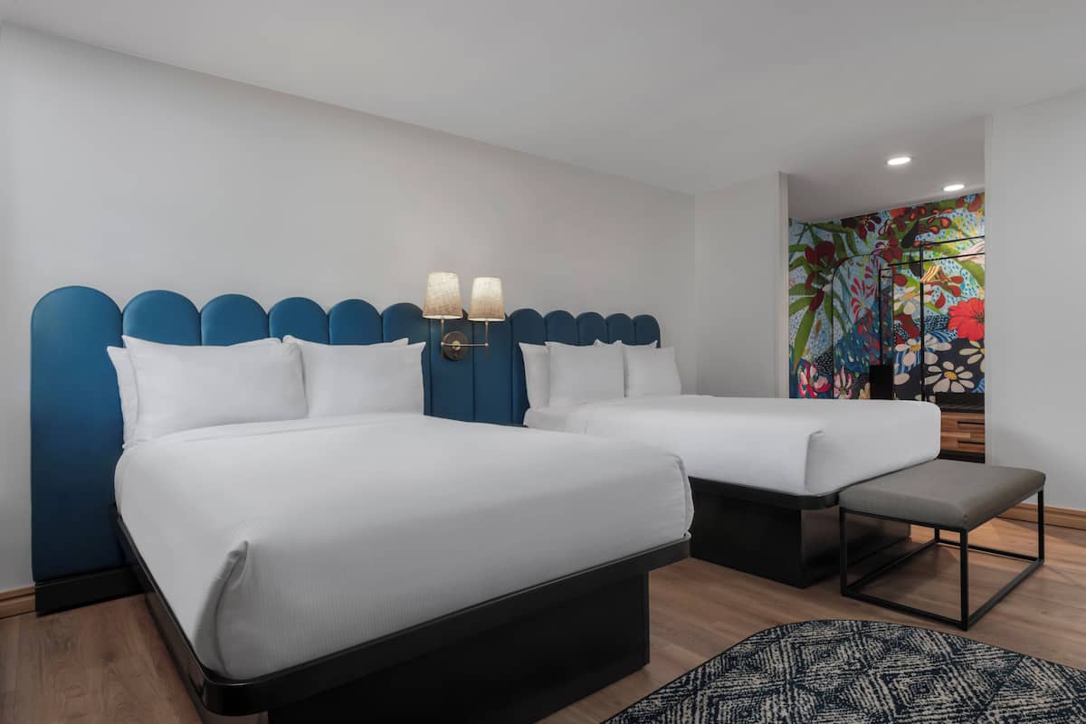 A hotel room with two beds, a bench, and a colorful floral wall mural.