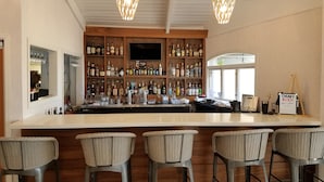 A bar area with a long counter, multiple shelves of bottles, a television, and wicker bar stools. - Catalina Canyon Inn (Avalon)