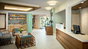 A reception area with a wooden reception desk, a computer, and a seating area with blue chairs and a table. - Catalina Canyon Inn (Avalon)