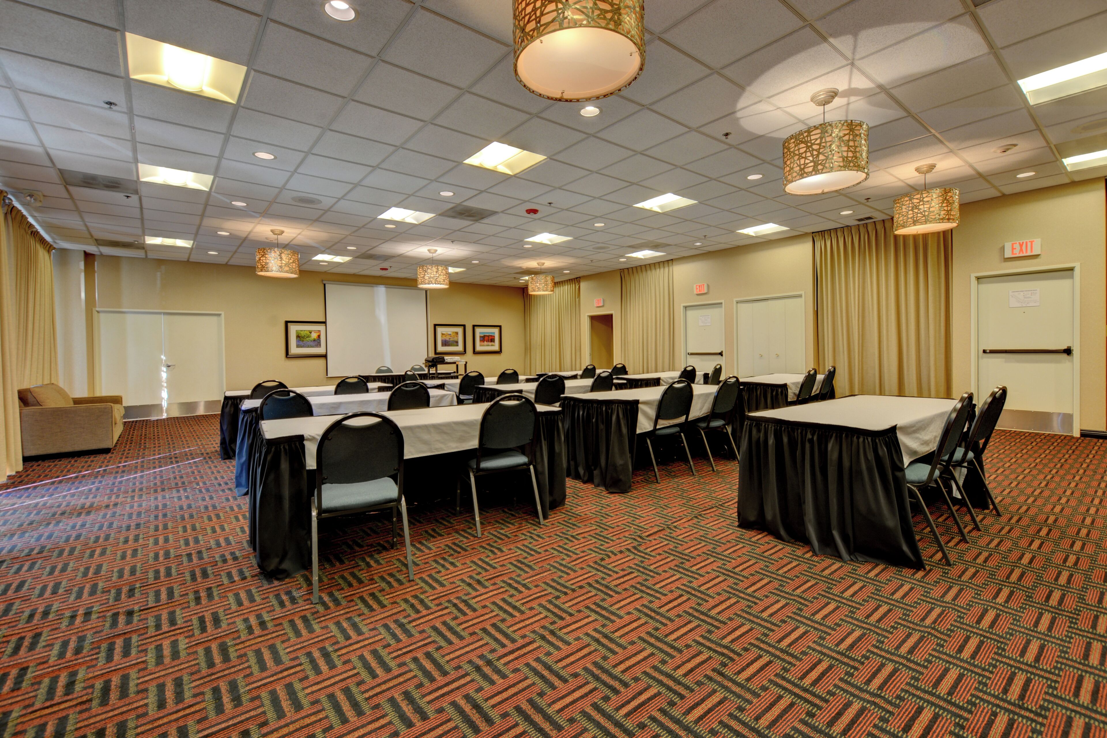 A conference room with tables and chairs, a projector screen, and an exit sign.