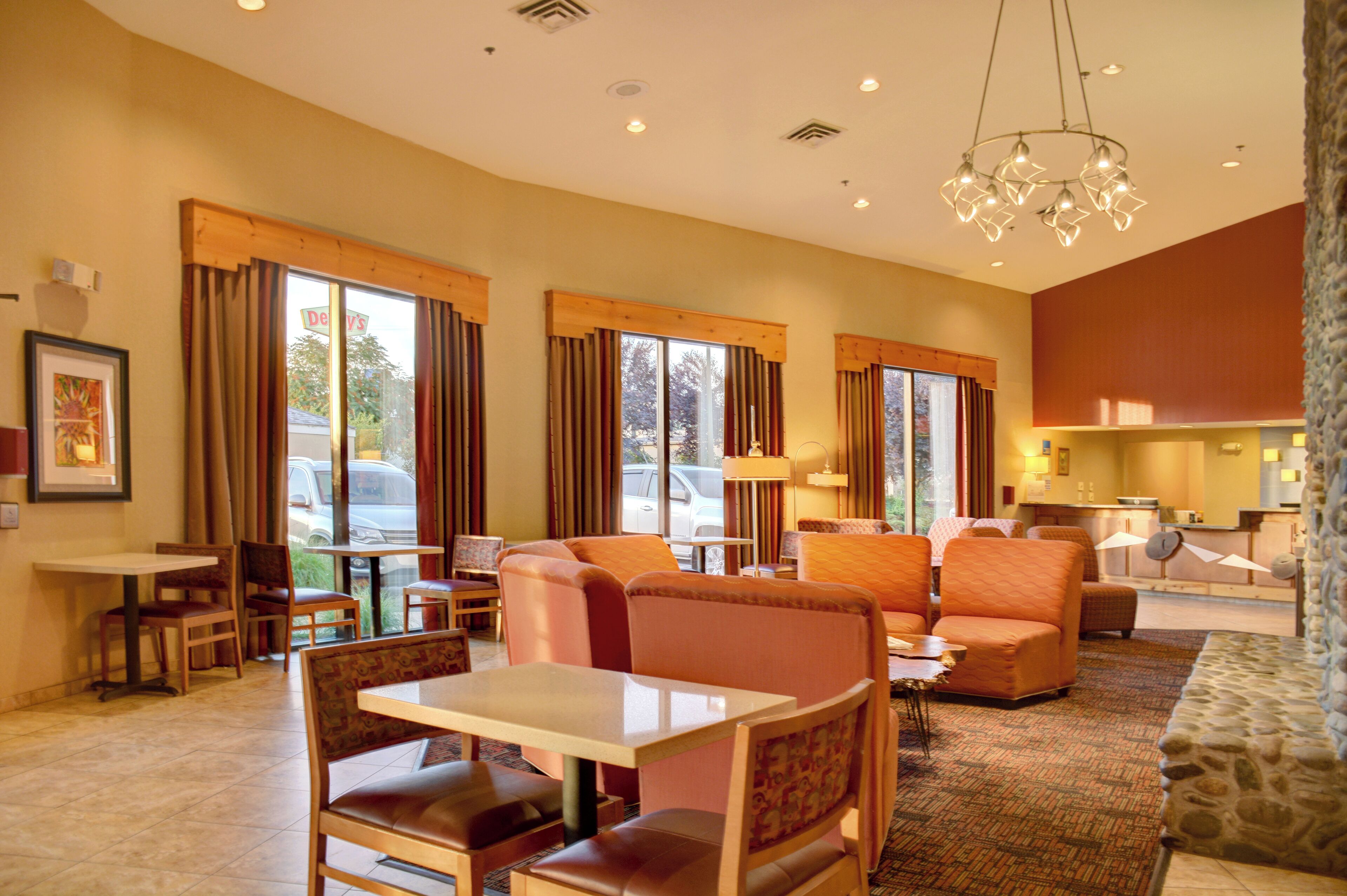 A hotel lobby with seating areas, a reception desk, and large windows with curtains.