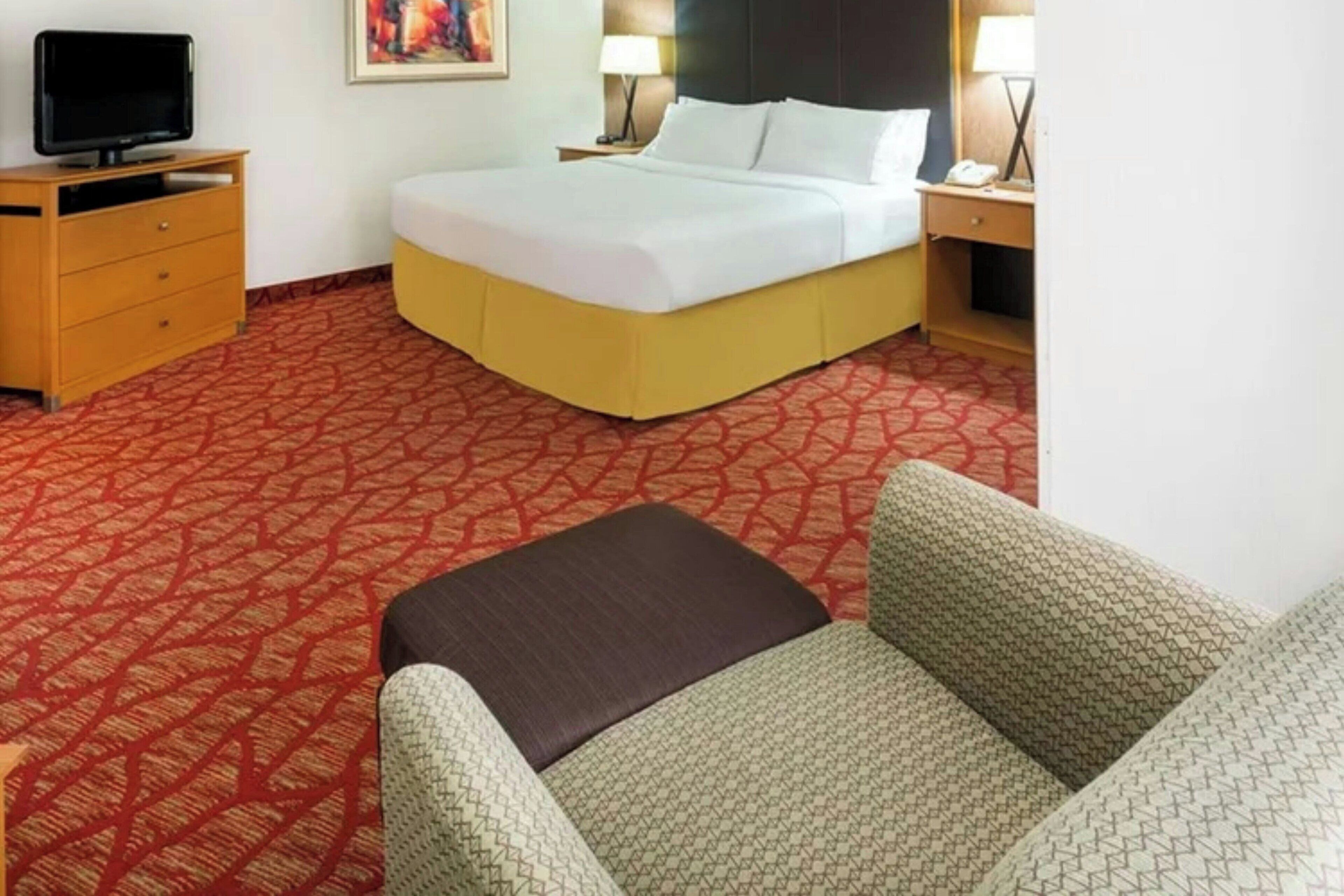 A hotel room with a bed, a TV, a desk, and a chair.