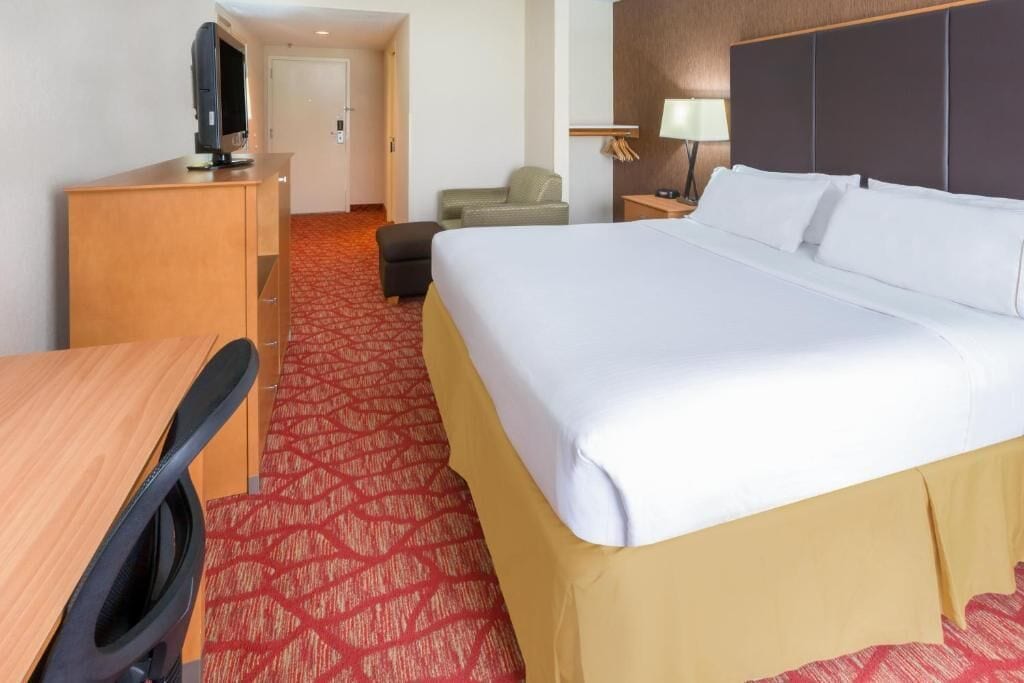 A hotel room with a bed, a desk, a chair, a TV, and a lamp.