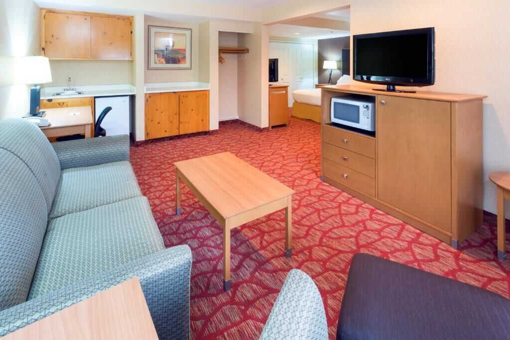 Ein Hotelzimmer mit einer Couch, einem kleinen Holztisch, einem Fernseher, einer Mikrowelle und einer Küchenzeile.