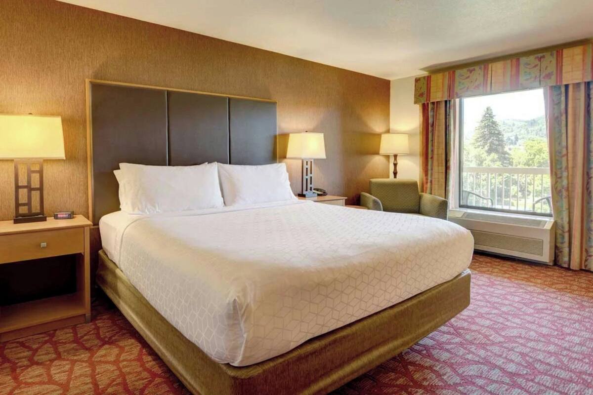 A hotel room with a large bed, two bedside tables, a chair, and a window with a view.