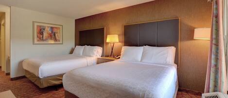 A hotel room with two beds, a painting on the wall, a lamp, and a heater.