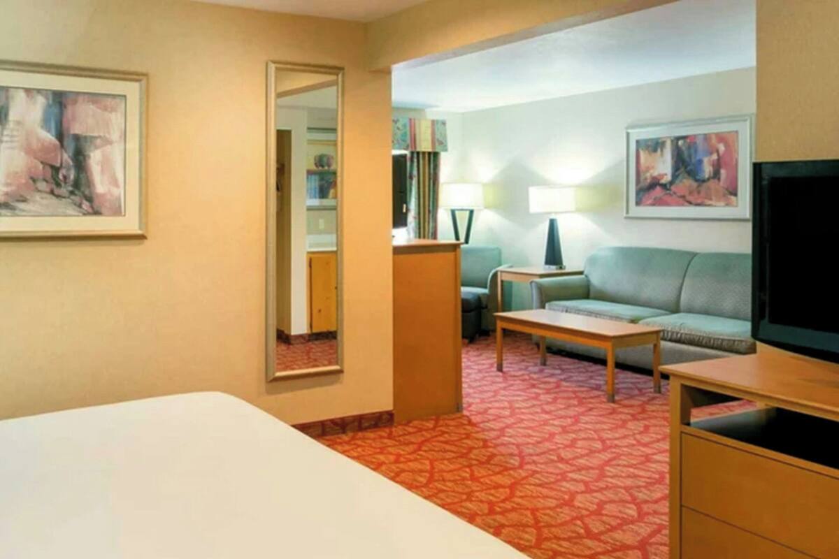A hotel room with a bed, a sofa, a TV, a lamp, and a mirror.